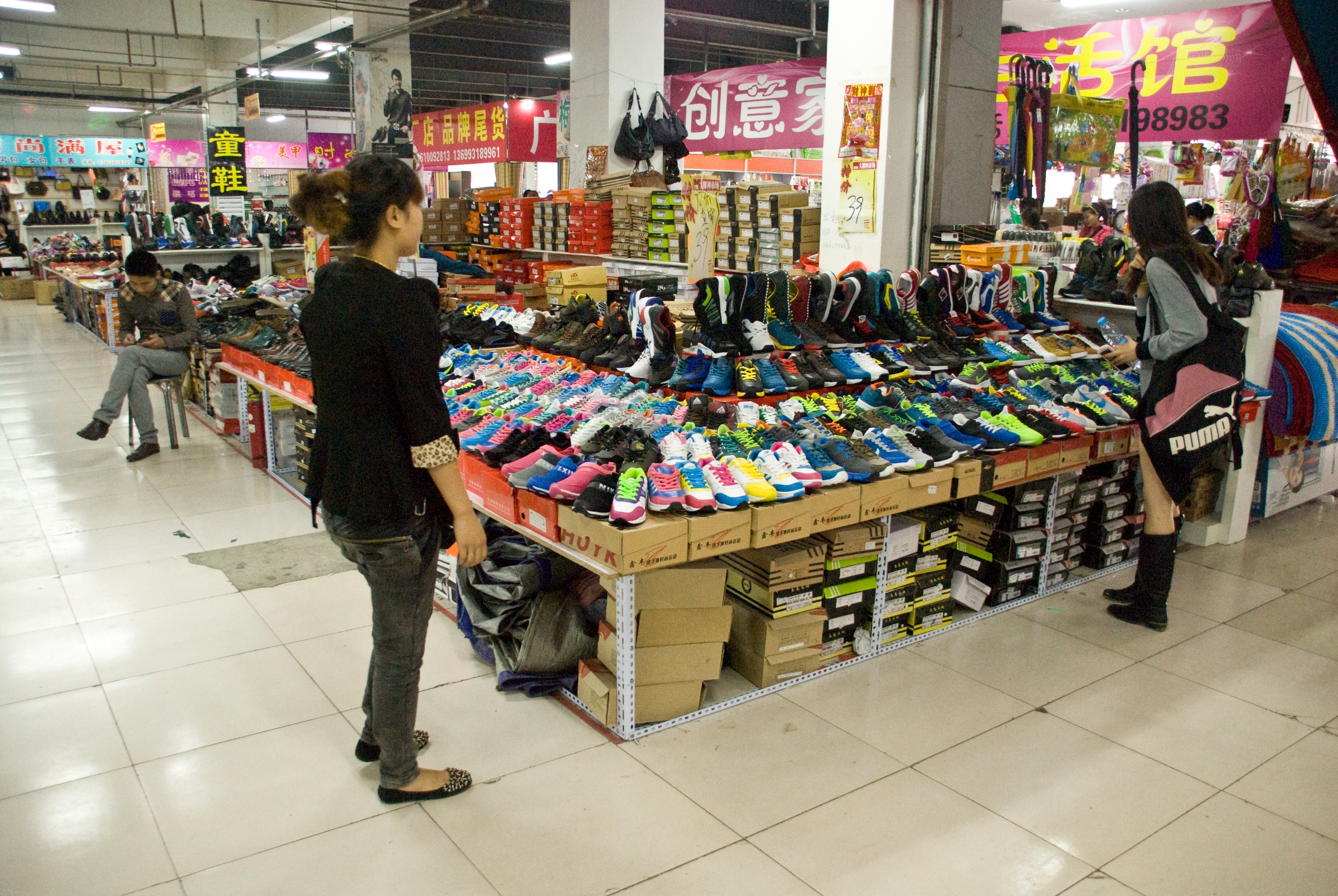 Colourful trainers displayed on stacked shoeboxes beneath Chinese signs in an indoor market, from the Dashilar Flagship Store project by Sander Wassink